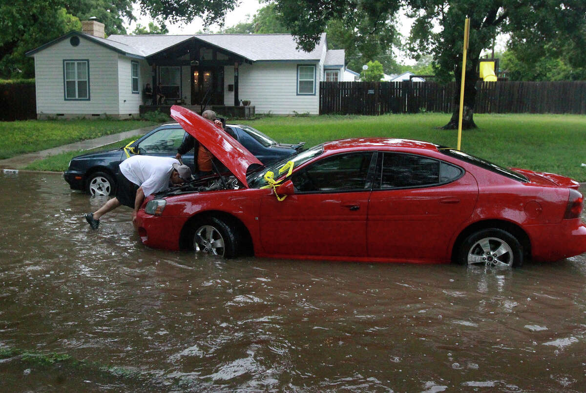 Raymond Martinez (under hood) prepares to have his car towed Wednesday June 25, 2014 at Brightwood Place and N. New Braunfels after stalling in high water.