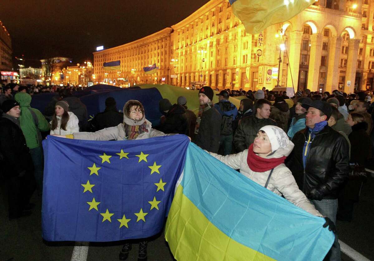 FILE - In this Tuesday Nov. 26, 2013 file photo, activists hold European Union, left, and Ukrainian flags during a meeting to support European Union integration at European Square in Kiev, Ukraine. On Friday, Ukraine will sign a sweeping economic and trade agreement with the European Union, a 1,200-page telephone book of a document crammed with rules on everything from turkeys to tulips, cheese to machinery. (AP Photo/Sergei Chuzavkov, File)