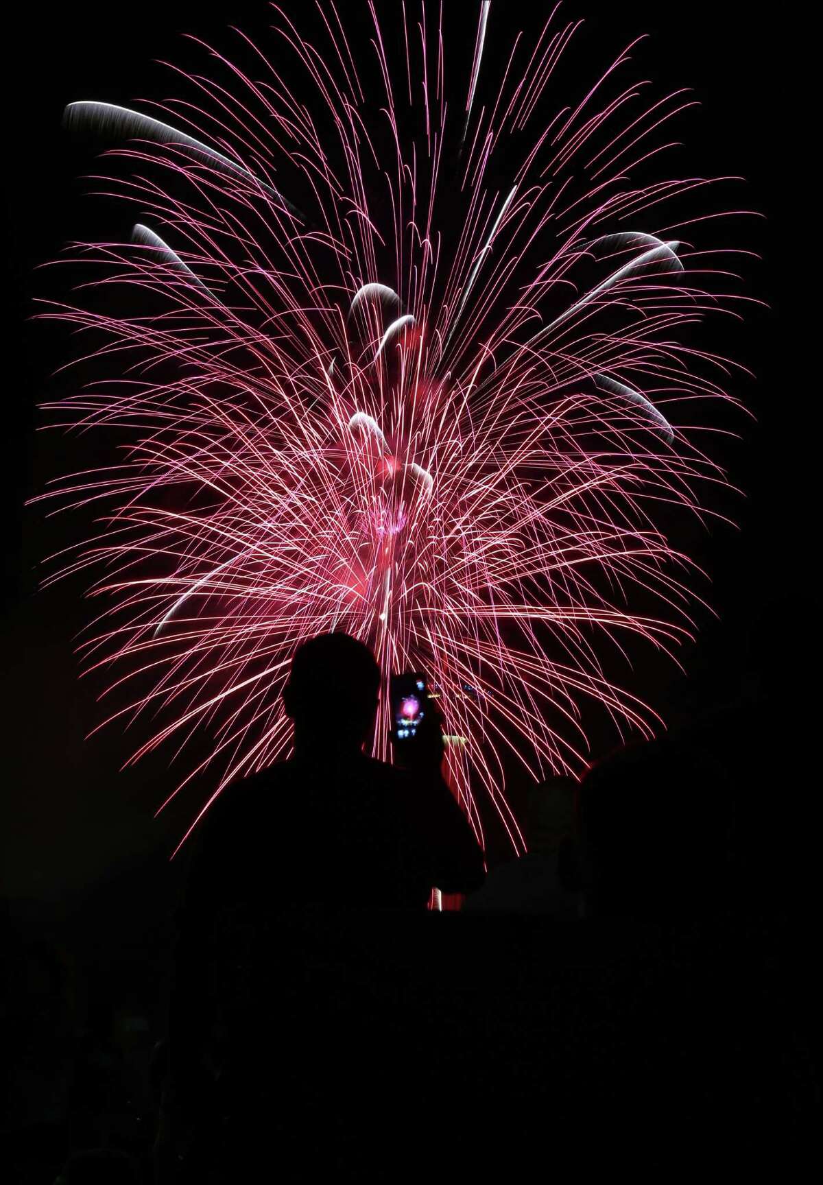 A man attending the Stars and Stripes on Thursday, July 4, 2014, at the Alamodome in San Antonio, records fireworks being set off from HemisFair Park.
