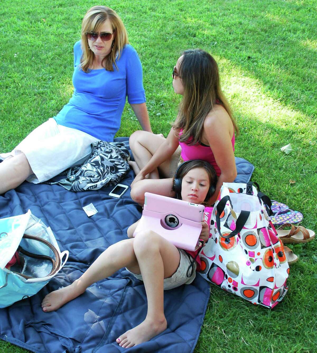 Sue Valentine, left, and Lorraine Plue, members of the WomanâÄôs Club of Greater New Milford, share some down time as LorraineâÄôs daughter, Alexis Plue, 8, indulges in her own pursuit before New MilfordâÄôs Fourth of July festivities kick off on the Village Green July 5, 2014. The Greater New Milford Chamber of Commerce spearheaded the festivities, which capped off with a fireworks display over the Fort Hill area. The Lions Club also sponsored a multi-day carnival at YoungâÄôs Field.