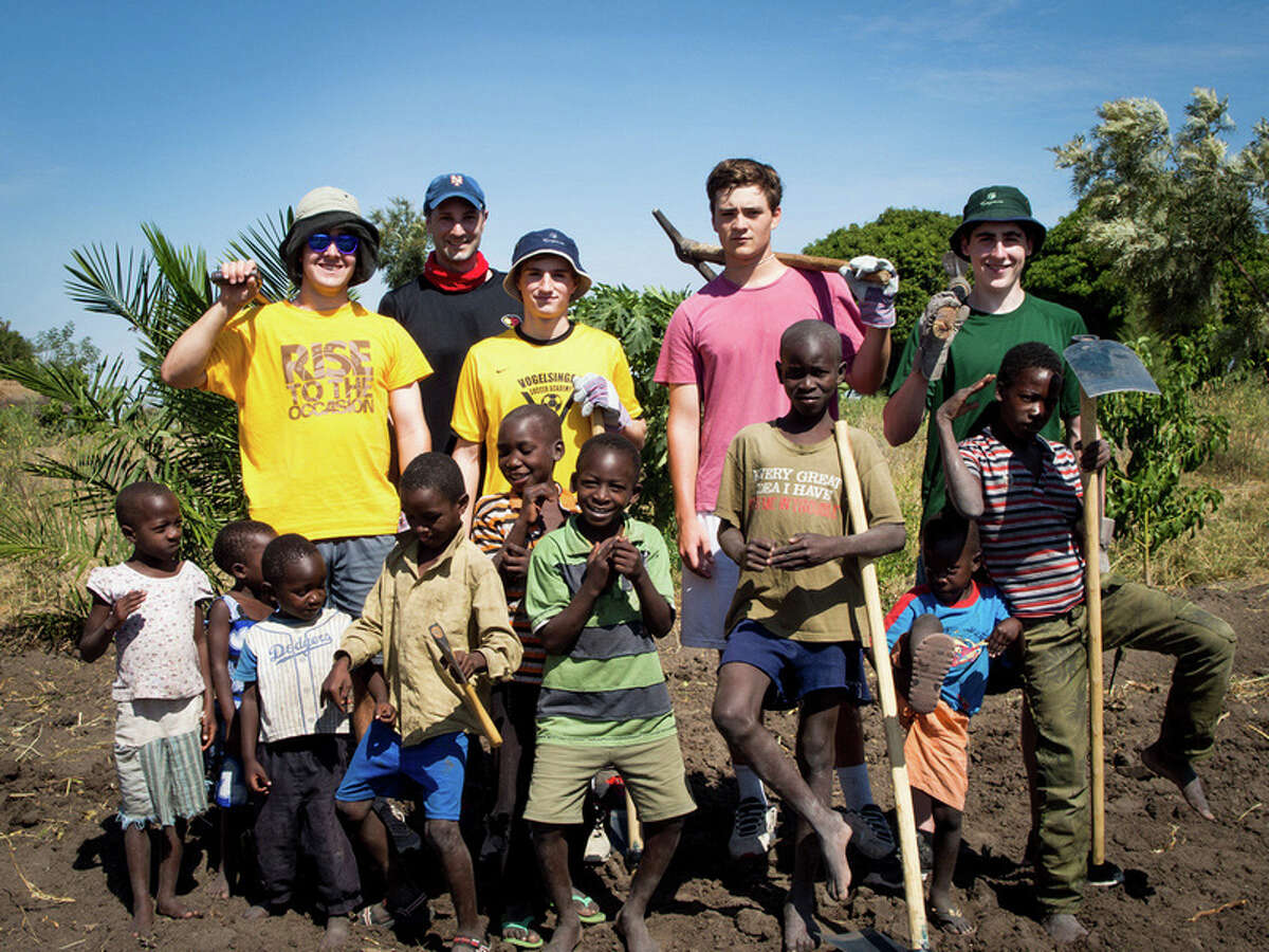 Brunswick School students (second row, left to right) Jamie MacFarlane of Greenwich, Dayton Kingery of Greenwich, Ryan Hanrahan of Bronxville, N.Y., and Jack Muccia of Rye, take a break from work in a Tanzanian farm field with native children and (rear) Brunswick environmental science teacher Dan Dychkowski. In June, the group traveled to the East African country to work at an orphanage for girls.