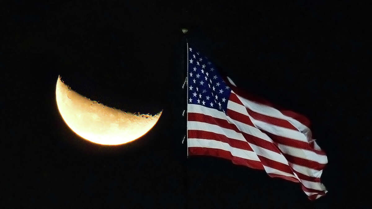A waning crescent moon rises over the stars and stripes at Allen Samuels Dodge on the Katy Freeway near Mason Rd. in the early morning hours of Saturday, Oct. 2, 2010, in Houston.