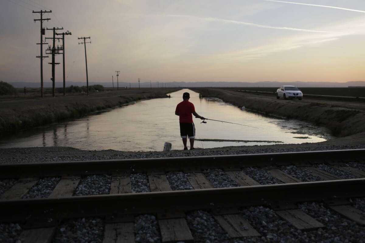 In this May 3, 2014 file photo, Rigoberto Arroyo, 18, fishes from a canal in Mendota, Calif. Throughout California's dry interior, those with water to spare are cashing in on the drought. As a third dry summer forces farmers to fallow fields and lay off workers, three water districts in the state's agricultural heartland are making millions of dollars by auctioning off their private, underground caches to the highest bidders.