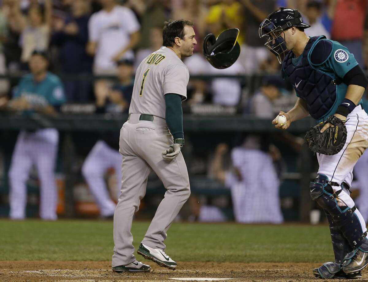 Oakland Athletics' Nick Punto's helmet bounces off the dirt in front of Seattle Mariners catcher Mike Zunino, right, after Punto threw it down when he was called out on strikes to end the ninth inning of a baseball game on Friday, July 11, 2014, in Seattle. The Mariners won 3-2. (AP Photo/Ted S. Warren)