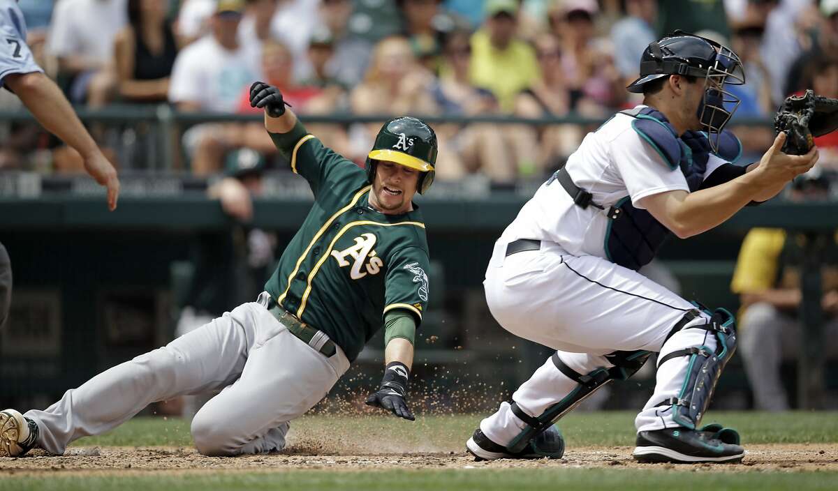 Oakland Athletics' Jed Lowrie, left, scores as Seattle Mariners catcher Mike Zunino waits for the ball in the fifth inning of a baseball game Sunday, July 13, 2014, in Seattle. (AP Photo/Elaine Thompson)