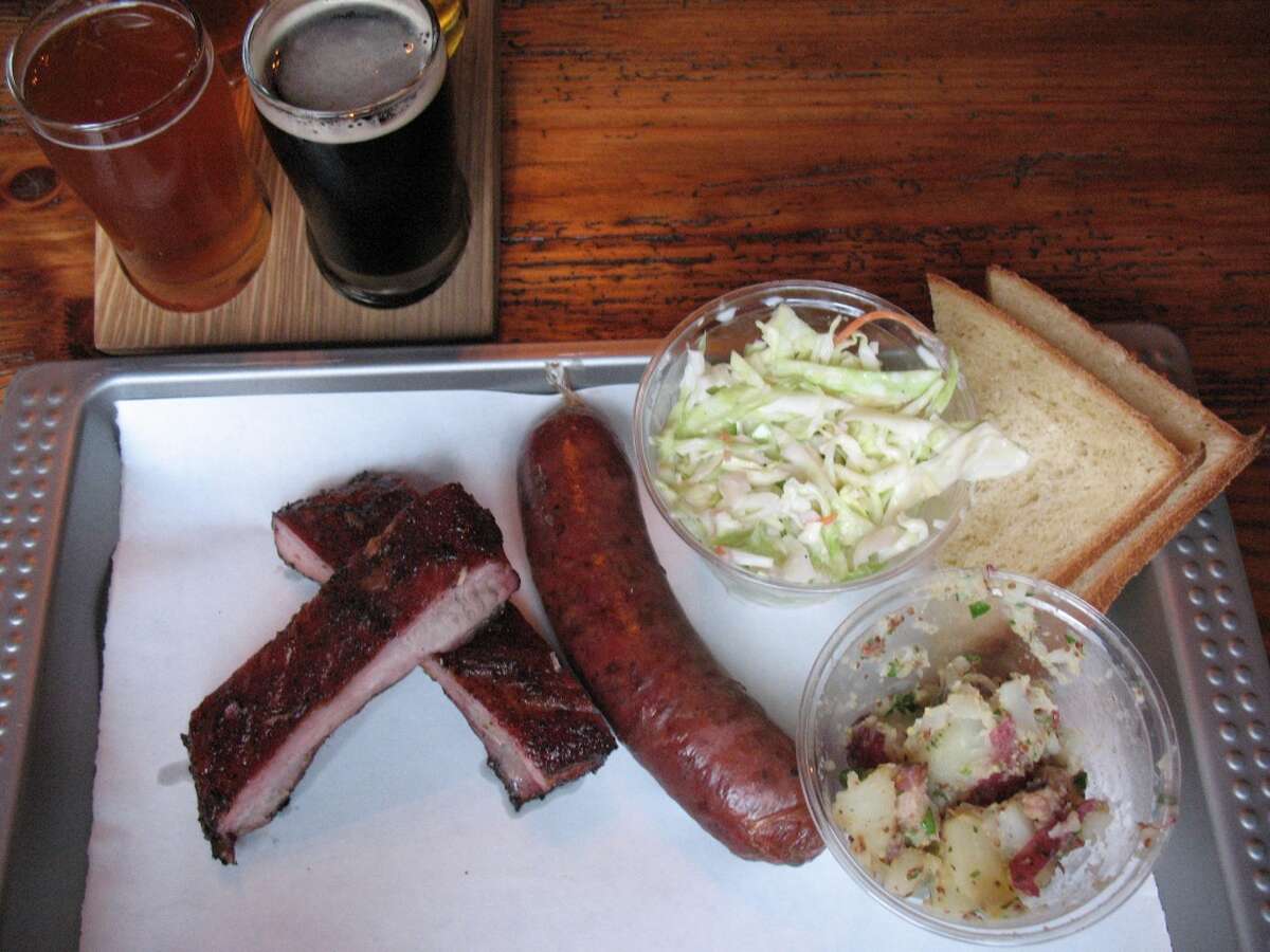 For SA Life Just a Taste: A two-meat lunch plate at The Granary with ribs and sausage and sides of cole slaw and German potato salad. Buttermilk bread is available separately. In the background is a flight of four house brews.