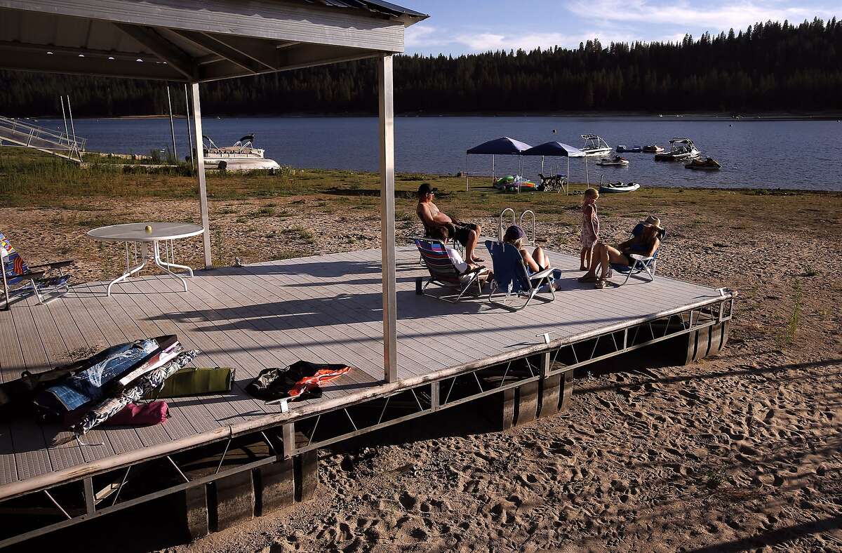 5-year-old Saylor Menna with her parents George and Sara Menna, of Santa Cruz relax along with Rachel Bartel, of Santa Cruz and Corky Roberson, of Scotts Valley, on their boat dock which would normally be afloat at Bass Lake on Thursday July 17, 2014, near Oakhurst, Calif. A prolonged drought could make it harder -- and more expensive -- for California to cut its greenhouse gas emissions and fight global warming. Drought cuts the amount of electricity that California gets from hydroelectric dams. To compensate, the state has to rely more on power plants burning natural gas.