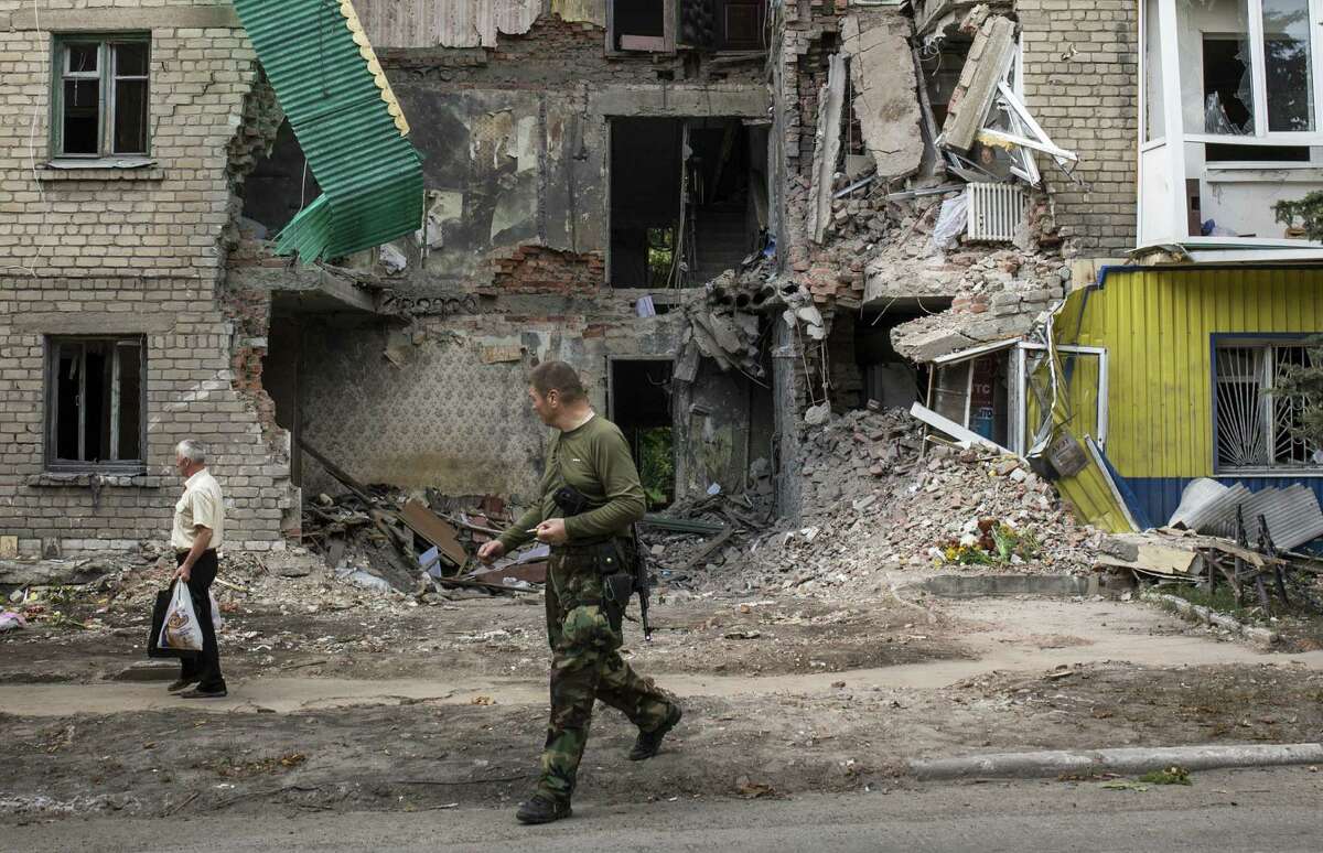 A pro-Russia rebel and a local resident walk past an apartment building recently damaged by rocket fire in Snizhne, Ukraine. Two Ukrainian military fighter jets were shot down by pro-Russian separatists in the eastern area of the country Wednesday.
