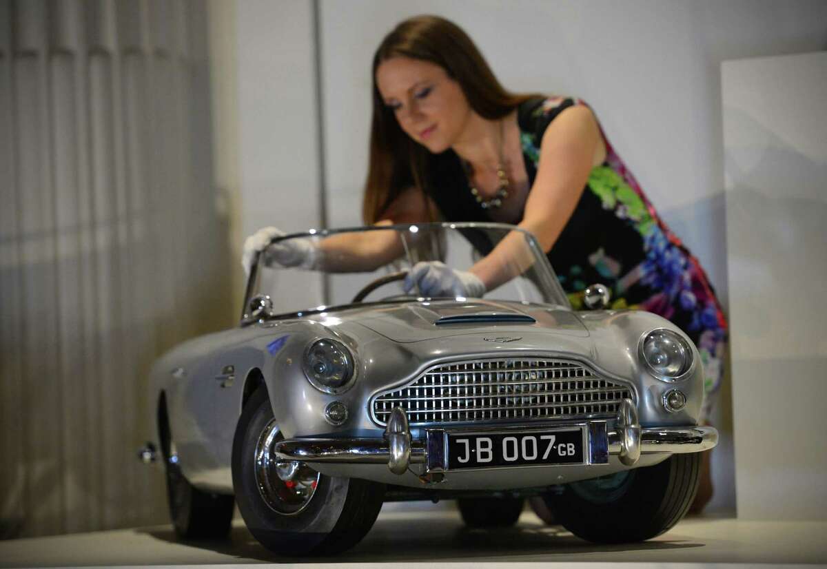 A member of staff poses for photographers with a miniature James Bond DB5 presented to Britain's Prince Andrew by the Aston Martin company in 1965, at Buckingham Palace in central London on July 24, 2014, during a preview for the forthcoming exhibition exploring 250 years of royal childhood. A special exhibition on childhood in the British royal family is to open at Buckingham Palace on Saturday, featuring well-loved toys spanning 250 years including a gadget-laden miniature James Bond supercar.