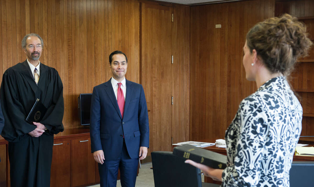 Julián Castro, center, prepares to be sworn in July 28, 2014 as the 16th Secretary for the U.S. Department of Housing and Urban Development. The brief swearing-in ceremony took place at HUD headquarters in Washington, D.C. and was administered by Chief Judge Richard W. Roberts, left, of the United States District Court for the District of Columbia. HUD Chief of Staff Nealin Parker, right, held the Bible during the ceremony.