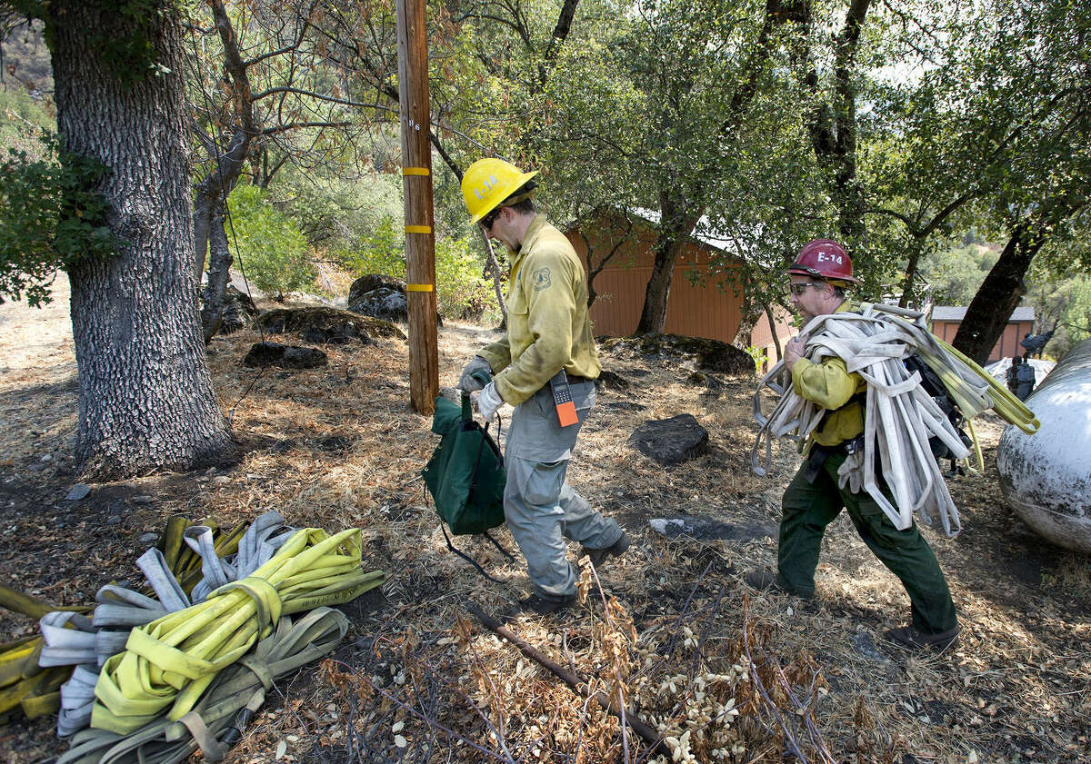 U.S. Forest Service firefighters Nick Parker (left) and Dwayne McGovran gather up hoses in the El Portal, Calif., community now that the homes are no longer threatened by wildfire.