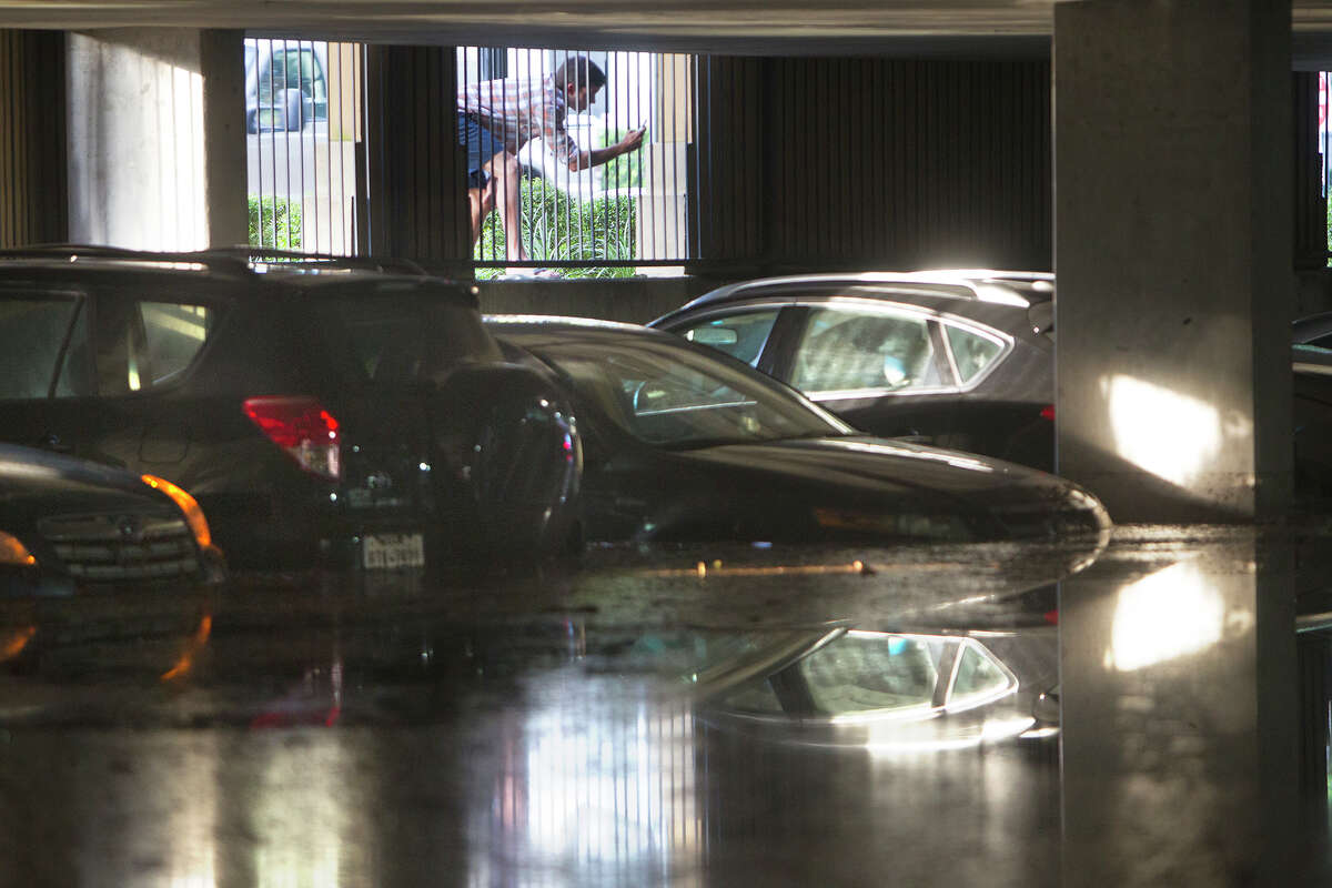 A man takes photos of cars as they sit in the Calais at Cortlandt Square apartment's parking garage after it flooded, Friday, Aug. 1, 2014, in Houston.