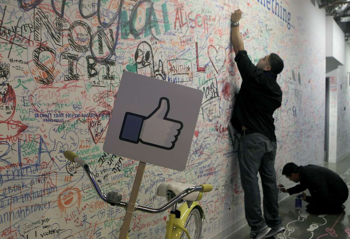 Mark Ryan stretches to write a message on a wall at a conference for small business owners at Facebook's headquarters in Menlo Park, Calif. on Tuesday, Aug. 5, 2014. 