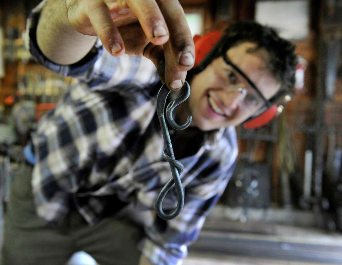 Nick Moreau shows off a hook that he has just crafted in his metal shop Tuesday, August 12, 2014. Nicholas Wicks Moreau, 26, of Westport, Conn., an artist blacksmith, uses his grandfather's old blacksmith shop in the garage of his family's Danbury home to do his work.