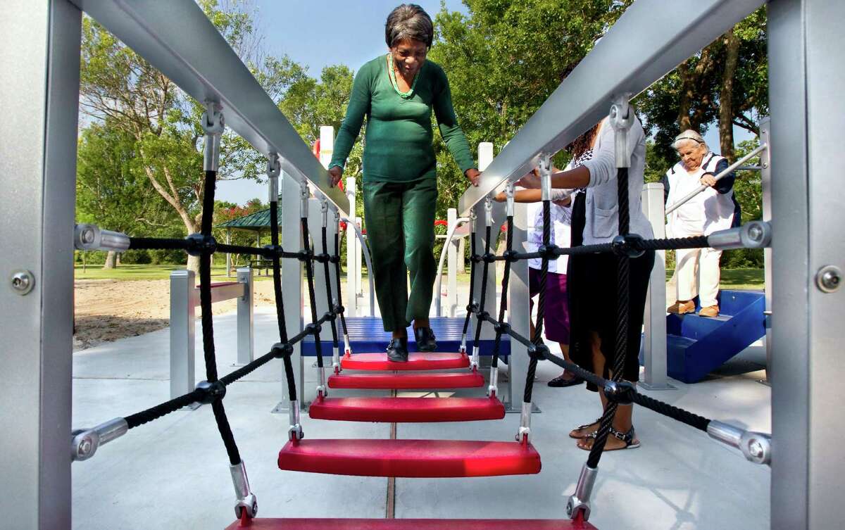 In this photo taken on Wednesday, Aug. 13, 2014, 84-year-old Zady Jones walks across a rope step bridge while trying out the new senior playground at Carbide Park in La Marque, Texas.