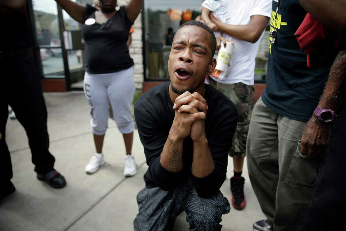 A man bends down in prayer as police try to disperse a small group of protesters Monday in Ferguson, Mo.