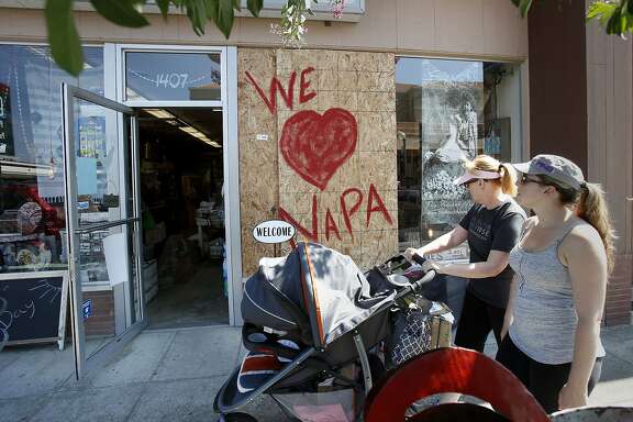 Two women pass a newly reopened store on Second Street advertising their love for Napa. Residents and shop owners in Napa, Calif. spent the day cleaning up or moving out after the large earthquake Sunday.
