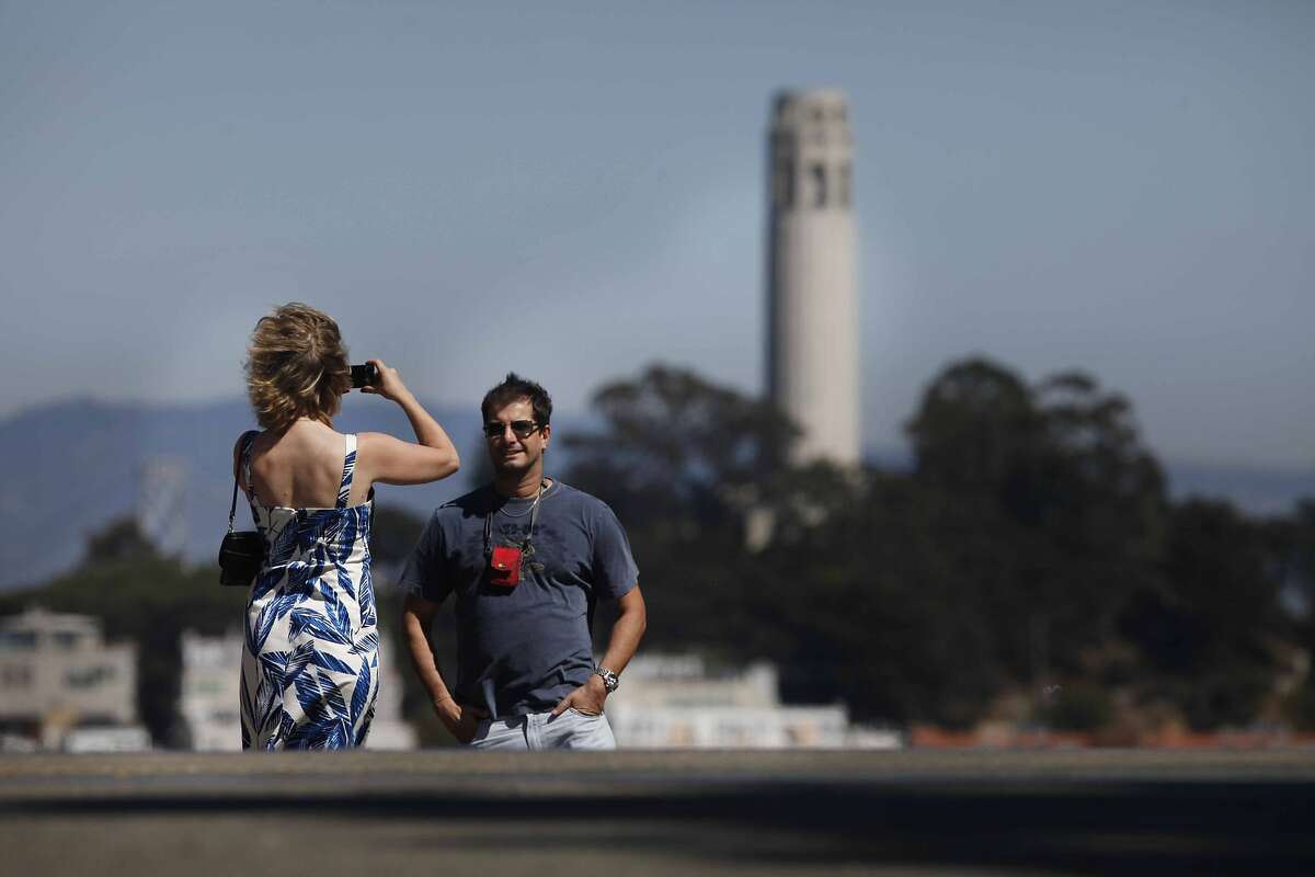Stopping for a quick snapshot, Tatiana Miranova and Roger Rezende join other tourists soaking up sun and views of Coit Tower at Hyde and Lombard Streets on Thursday Sep. 9, 2009 in San Francisco, Calif.