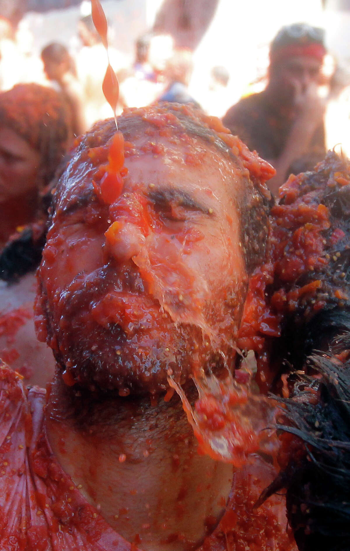 A man reacts as he is hit with tomatoes, during the annual "tomatina" tomato fight fiesta in the village of Bunol, 50 kilometers outside Valencia, Spain, Wednesday, Aug. 27, 2014. The streets of an eastern Spanish town are awash with red pulp as thousands of people pelt each other with tomatoes in the annual "Tomatina" battle that has become a major tourist attraction. At the annual fiesta in Bunol on Wednesday, trucks dumped 125 tons of ripe tomatoes for some 22,000 participants, many from abroad to throw during the hour-long morning festivities.