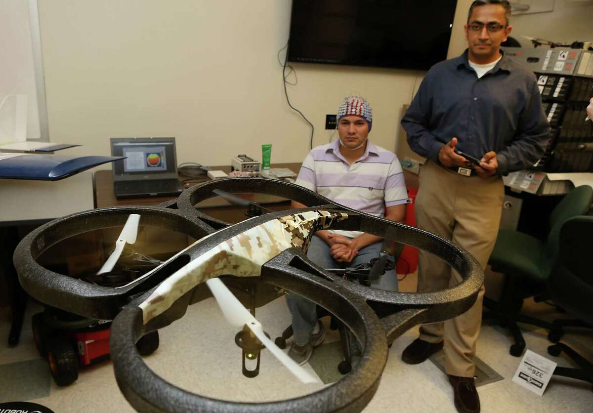 Prasanna Kolar, right, a masters student in Computer Engineering at UTSA, controls a quad copter through an app on his smart phone. Kolar and other students at UTSA's Electrical and Computer Engineering Department are studying how to control a drone with brain waves collected by the electroencephalogram system (cap) worn by Mauricio Merino, a masters student in Electrical Engineering. A grant from the Department of Defense will enable UTSA's drone researchers to acquire two state-of-the-art systems to analyze brain waves and applying that knowledge to control drones with brain waves. Wednesday, August. 27, 2014.