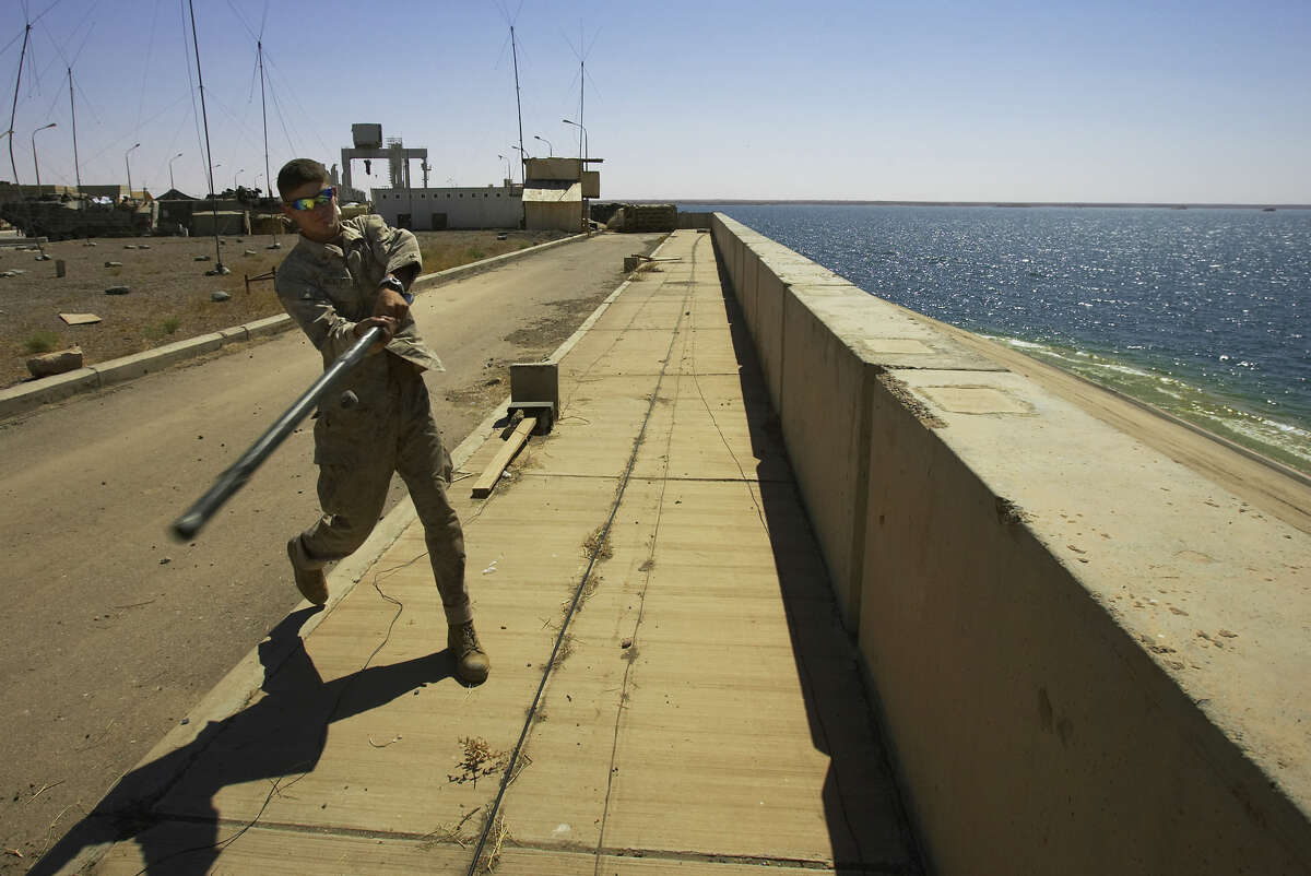 FILE - In this Sunday, May 29, 2005 file photo, U.S. Marine Lance Cpl. Andrew Bickerstaff of Satellite Beach, Florida, uses a tent pole to bat a rock off the Haditha Dam where his unit is based, 220 kilometers (140 miles) northwest of Baghdad. The U.S. military launched airstrikes Sunday around Haditha Dam in western Iraq, targeting Islamic State insurgents there for the first time in a move to prevent the group from capturing the vital dam. (AP Photo/Jacob Silberberg, File)