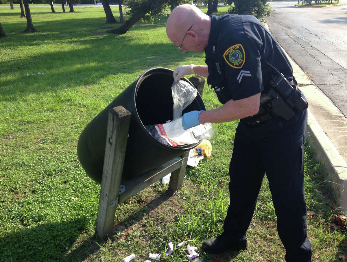 A Houston police officer investigates dozens of armored car bags found in a trash bin Sunday morning near the picnic area in MacGregor Park.