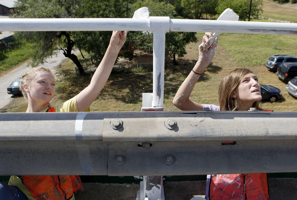 Stephanie Stockwell, 15, (left) and Kylee Caldwell, 13, paint the railing on the Guadalupe Street bridge near South Frio Street.