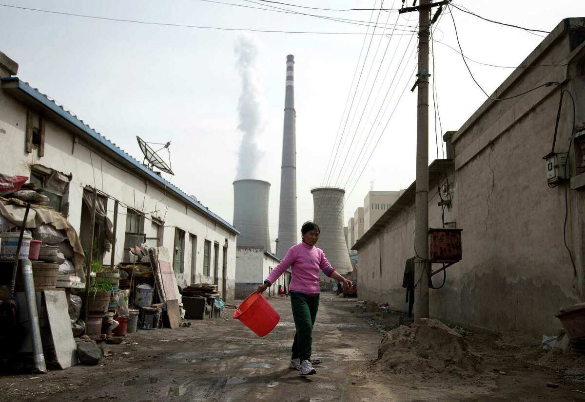 FILE - In this April 12, 2013 file photo, a woman walks through a neighborhood near a coal-fired power plant in Beijing. Carbon dioxide levels in the atmosphere reached a record high in 2013 as increasing levels of man-made pollution transform the planet, the U.N. weather agency said Tuesday, Sept. 9, 2014. (AP Photo/Andy Wong, File)