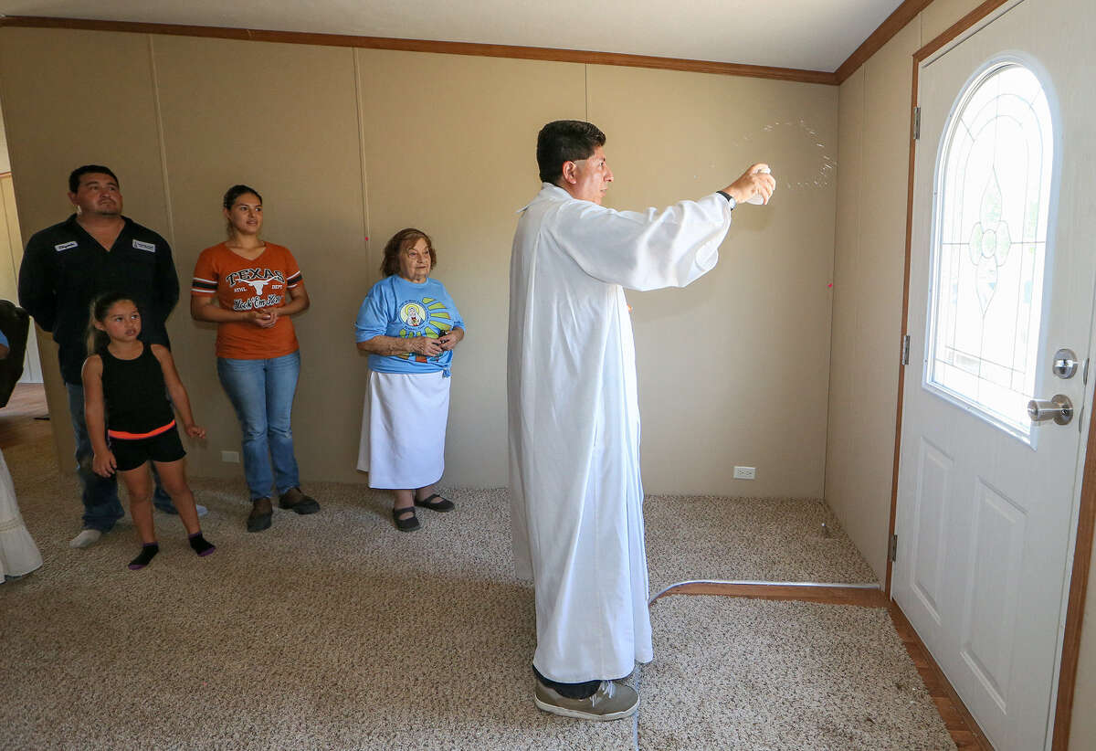 Father Jesús Camacho, pastor of Immaculate Heart of Mary Catholic Church in Pearsall, sprinkles holy water as he blesses the home of James and Crystal Elizondo (left), standing with their daughter Leileneo Cuevas, 5, and Alma Salinas. Members of the congregation also went door to door to invite people to attend Mass.