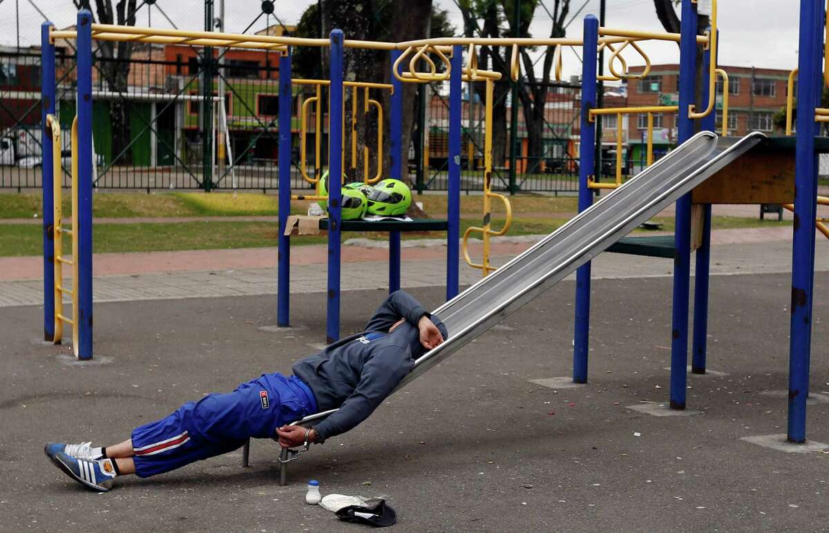 A detainee rests, handcuffed to a slide, at a children's playground in a public park in Bogota, Colombia, Thursday, Sept. 11, 2014. Due to overcrowding at a detention center located across the street, the park has been converted into makeshift holding area, where detainees, most accused of petty crimes, are kept for days waiting for a prosecutor's decision.