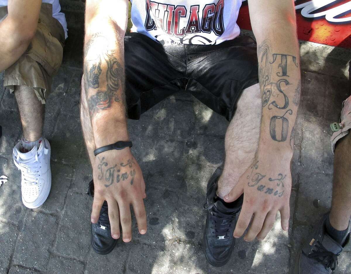 In this Sept. 5, 2014 photo, a reputed member of the Los Solidos street gang shows his tattoos to police in Hartford, Conn. The TSO and theater mask on his left arm are tell-tale signs of Los Solidos. TSO means The Solid Ones, the English translation of Los Solidos. Despite the tattoos, gang members are shying away from wearing their colors in an effort to avoid being detected by authorities, police said. (AP Photo/Dave Collins)