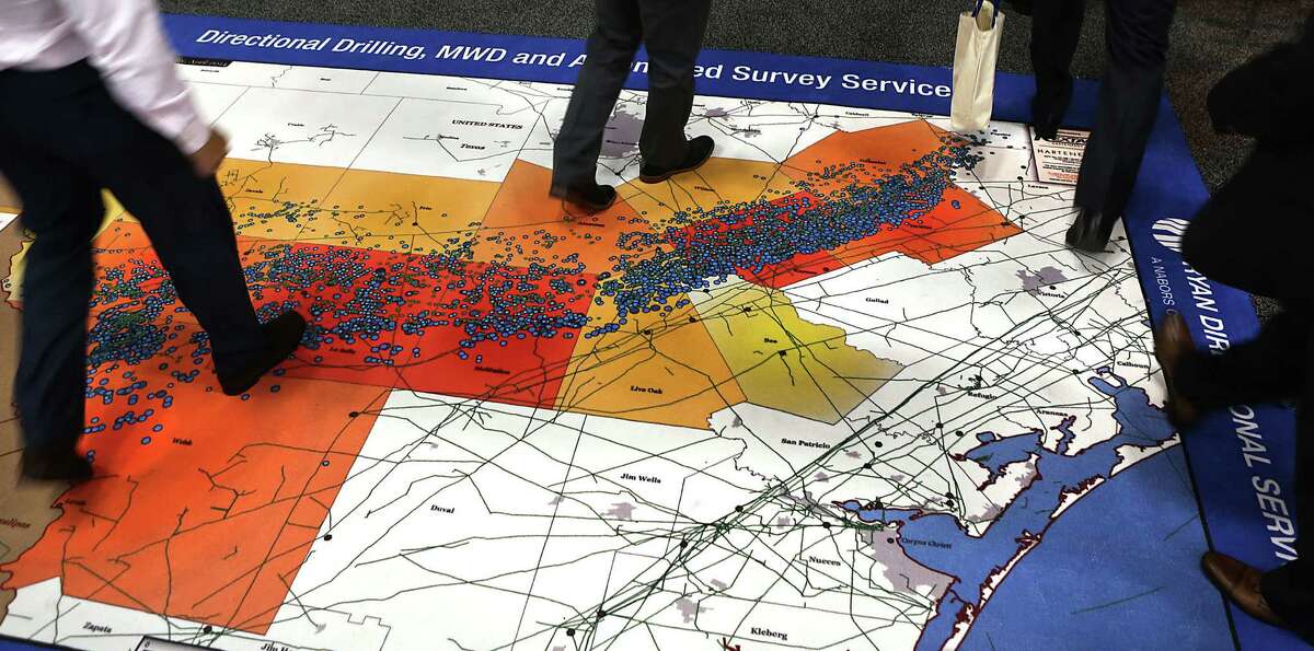 Workers from the oil and gas industry walk across a map showing Eagle Ford well activity in South Texas.