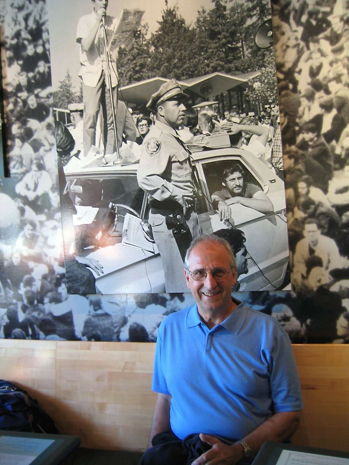 Jack Weinberg in front of a photo of him in the police car, taken at the Free Speech Movement Cafe on the UC Berkeley campus