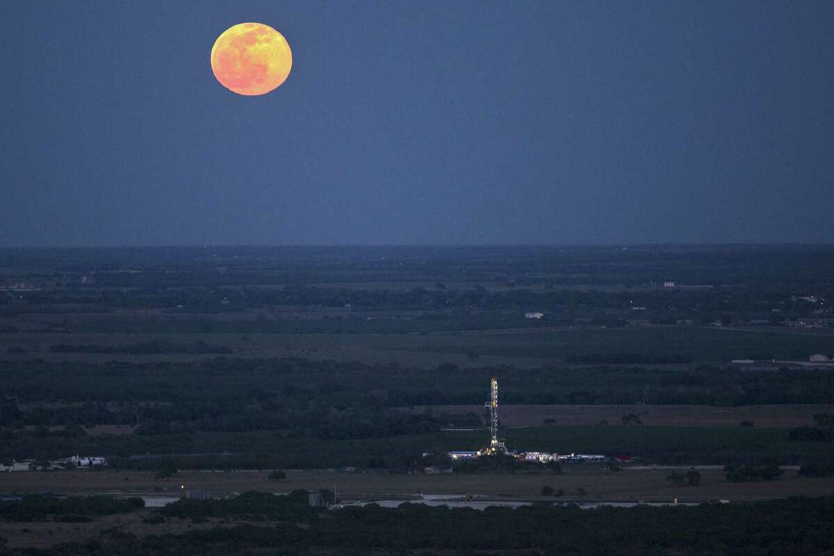 The full moon rises above an oil drilling rig Wednesday, May 14, 2014 in an aerial image taken near Karnes City, Texas.