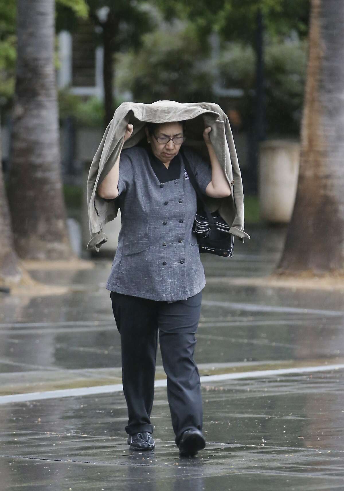 A woman covers her head during the first rain of autumn in Sacramento, Calif., Thursday, Sept. 25, 2014. While the brief storm is not expected to do much to improve the drought situation in California, it is welcome relief by fire fighters battling the King fire that has burned more than 90,000 acres in the nearby Sierra Nevada foothills.