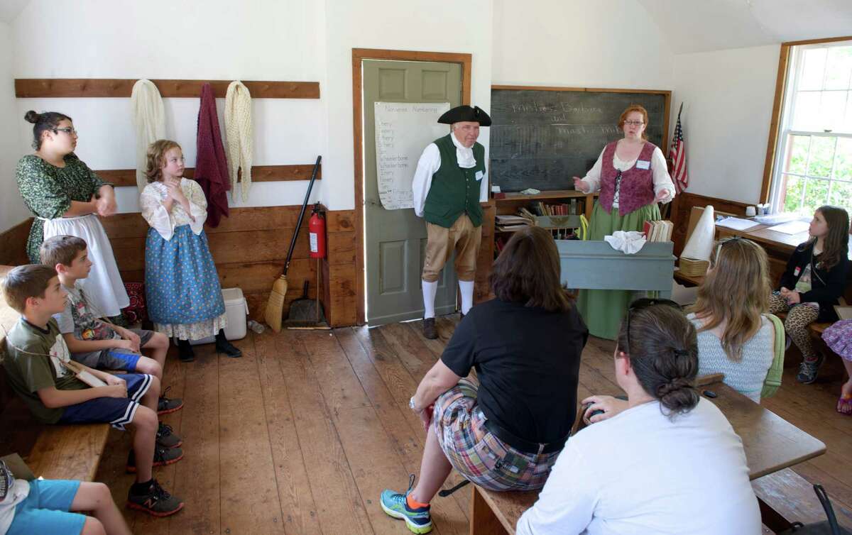Barbara Wilson, 51, of Newtown, dressed in colonial costume, talks to a group of children and their parents about school life during colonial times for the Newtown Historical Society's annual Children's Day at the Little Red School House on the grounds of Middle Gate School in Newtown, Conn., on Sunday, Sept. 28, 2014. Standing next to Wilson is Michael Asselta, 80, of Sandy Hook.