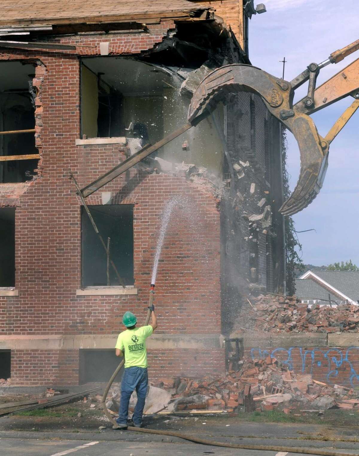 The demolition of Danbury Hall is underway at Fairfield Hills in Newtown, Conn. Julio Argueta keeps the water flowing to control the dust from the debris as an excavator run by Andy Bowolick, wacks the side of the building, Monday, Sept. 29, 2014.