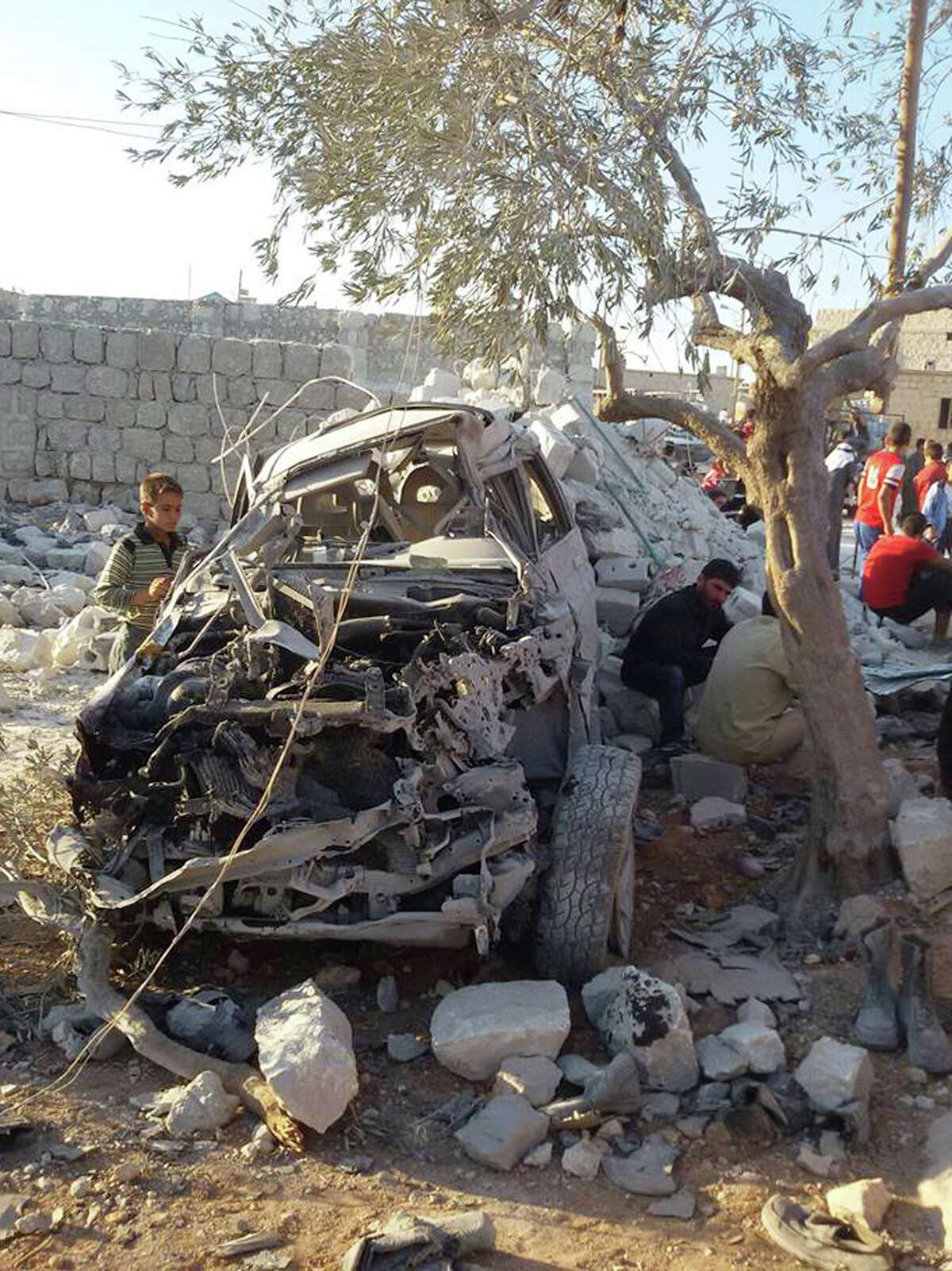 This photo provided by an anti-Bashar Assad activist group Edlib News Network (ENN), which has been authenticated based on its contents and other AP reporting, shows a Syrian boy, left, looking at a destroyed car that activists say was targeted by the coalition airstrikes, in the village of Kfar Derian, a base for the al-Qaida-linked Nusra Front, a rival of the Islamic State group, between the northern province of Aleppo and Idlib, Syria, Tuesday Sept. 23, 2014. Syria said Tuesday that Washington informed President Bashar Assad's government of imminent U.S. airstrikes against the Islamic State group, hours before an American-led military coalition pounded the extremists' strongholds across northern and eastern Syria. (AP Photo/Edlib News Network ENN)