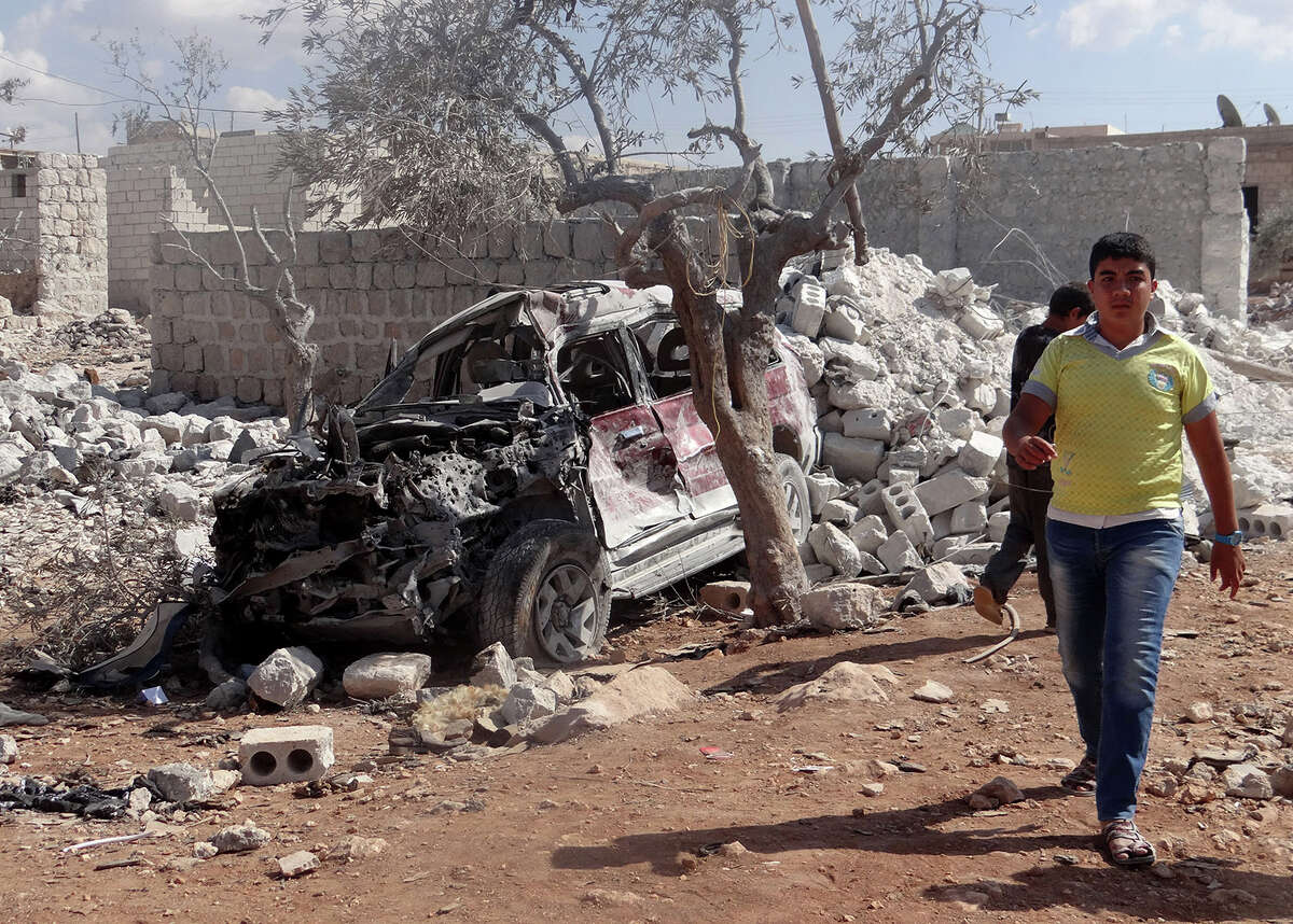 A Syrian youth walks past the wreckage of a vehicle following the U.S.-led coalition's airstrikes against the Islamic State of Iraq and the Levant (ISIL) on a residential area in Idlib, Syria on September 23, 2014.