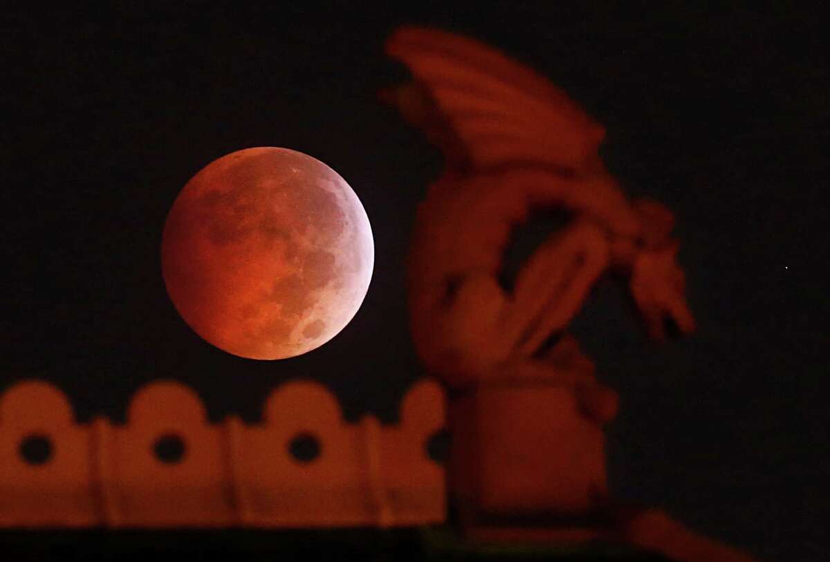 A lunar eclipse appears behind a gargoyle atop the old red Dallas County Courthouse early Wednesday morning, Oct. 8, 2014. The moon appears orange or red, the result of sunlight scattering off Earth's atmosphere. This is known as the blood moon. (AP Photo/The Dallas Morning News, Tom Fox) MANDATORY CREDIT; MAGS OUT; TV OUT; INTERNET USE BY AP MEMBERS ONLY; NO SALES