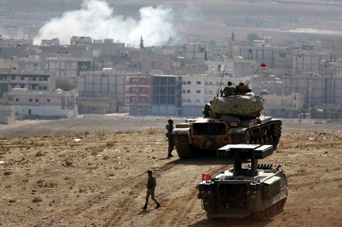 Turkish soldiers, with a tank and an armored vehicle, occupy a border hilltop overlooking Kobani, Syria.