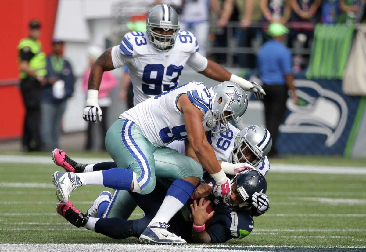 Seattle Seahawks quarterback Russell Wilson, bottom, is sacked by Dallas Cowboys defensive end George Selvie (99) and Tyrone Crawford (98) in the first half of an NFL football game, Sunday, Oct. 12, 2014, in Seattle. (AP Photo/Elaine Thompson)