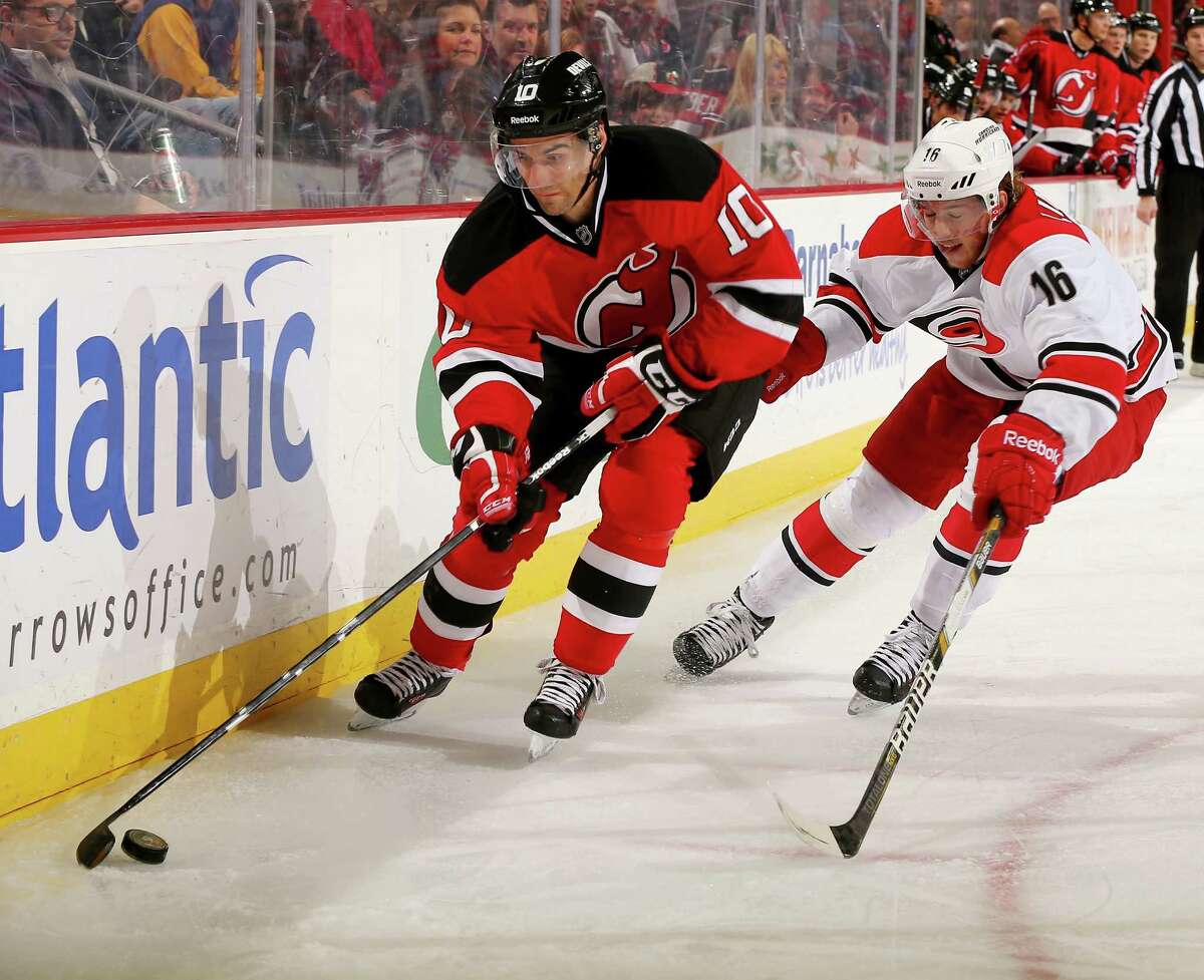 NEWARK, NJ - NOVEMBER 27: Peter Harrold #10 of the New Jersey Devils tries to keep the puck from Elias Lindholm #16 of the Carolina Hurricanes at Prudential Center on November 27, 2013 in Newark, New Jersey. (Photo by Elsa/Getty Images) ORG XMIT: 181111247