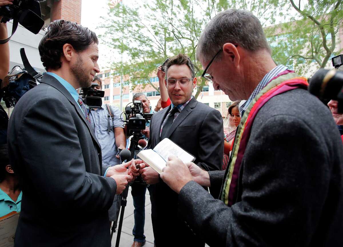 Kevin Patterson, left, and David Larance exchange vows by Rev. Dr. John Dorhaer, right, Friday, Oct. 17, 2014, in Phoenix. Gay marriage has become legal in Arizona after the state's conservative attorney general said Friday that he wouldn't challenge a federal court decision that cleared the way for same-sex unions in the state. (AP Photo/Rick Scuteri)