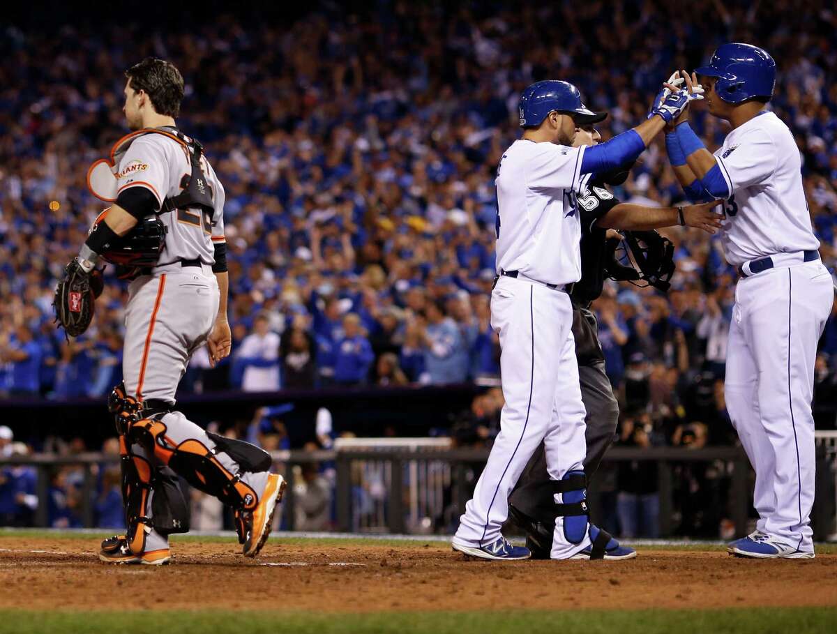 San Francisco Giants catcher Buster Posey walks past as Kansas City Royals Salvador Perez, right, congratulates teammate Omar Infante after Infante's two-run home run during the sixth inning of Game 2 of baseball's World Series Wednesday, Oct. 22, 2014, in Kansas City, Mo. (AP Photo/Matt Slocum)