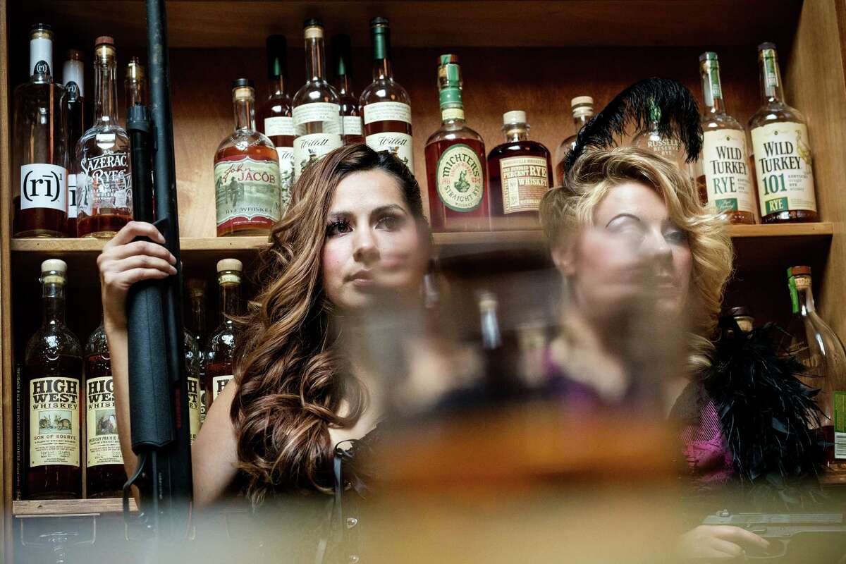 Models Kailey Anne Sommerdorf, 20, right, and Marlene Rodriguez, 27, left, patiently hold their pose as Seattle artist Ethan Harrington paints them for his 10-years-and-counting project, "Whiskey Women," as photographed Thursday, Oct. 23, 2014, at The Whiskey Bar in Seattle. Since 2004, Harrington has painted over 60 different women within The Whiskey Bar, which will host a showing his pieces on Nov. 5, 2014. The show is open to the public.