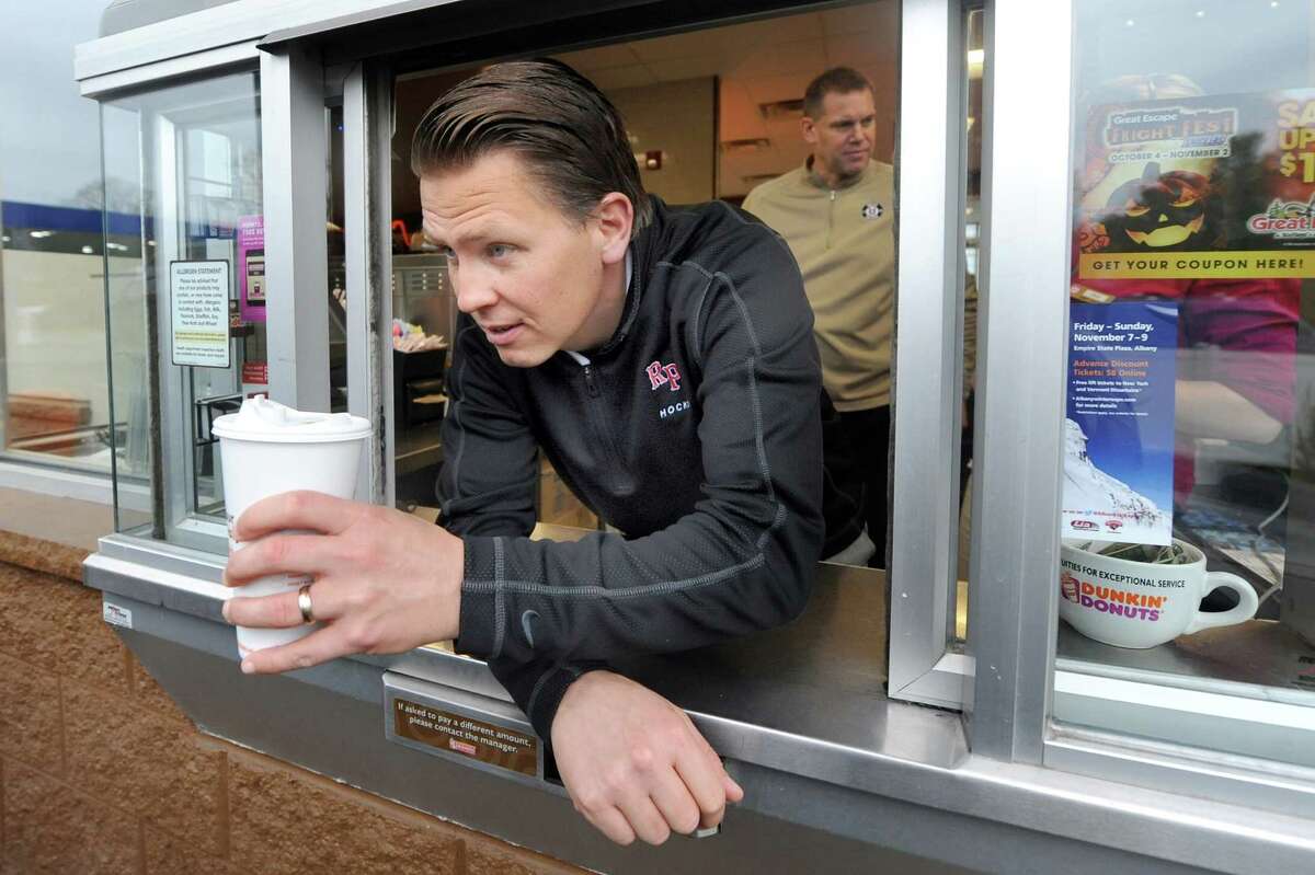 RPI hockey coach Seth Appert hands off a coffee in the drive through on Wednesday, Oct. 29, 2014, at Dunkina Donuts in Latham, N.Y. Coach Appert and Union hockey coach Rick Bennett, in the background, renew their Route 7 Rivalry as they promote their upcoming hockey games against each other. (Cindy Schultz / Times Union)