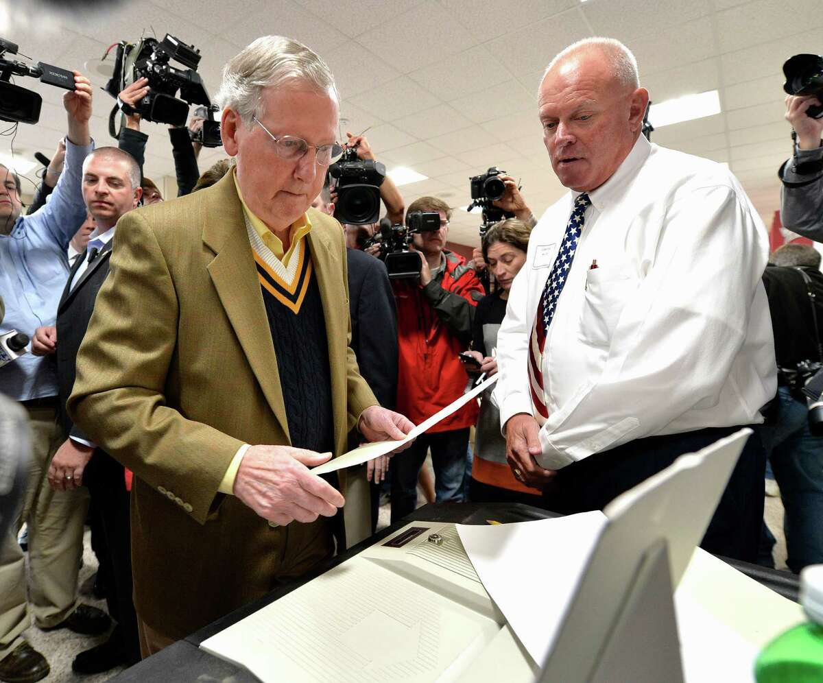 Senate Minority Leader Mitch McConnell of Ky., left, casts his vote as poll worker William Comstock looks on in Louisville, Ky., Tuesday, Nov. 4, 2014. (AP Photo/Timothy D. Easley)