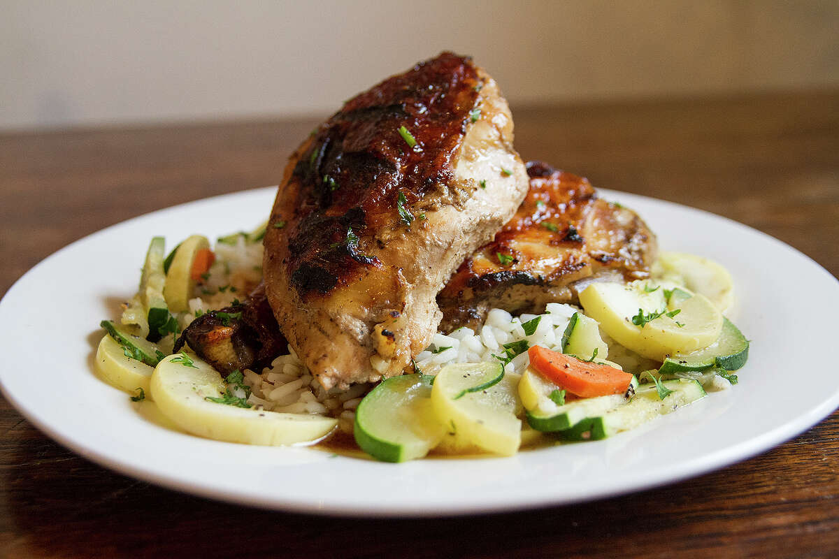 A dinner item of roasted chicken is served on a bed of rice pilaf with a veggie medley of squash, zucchini and carrots.