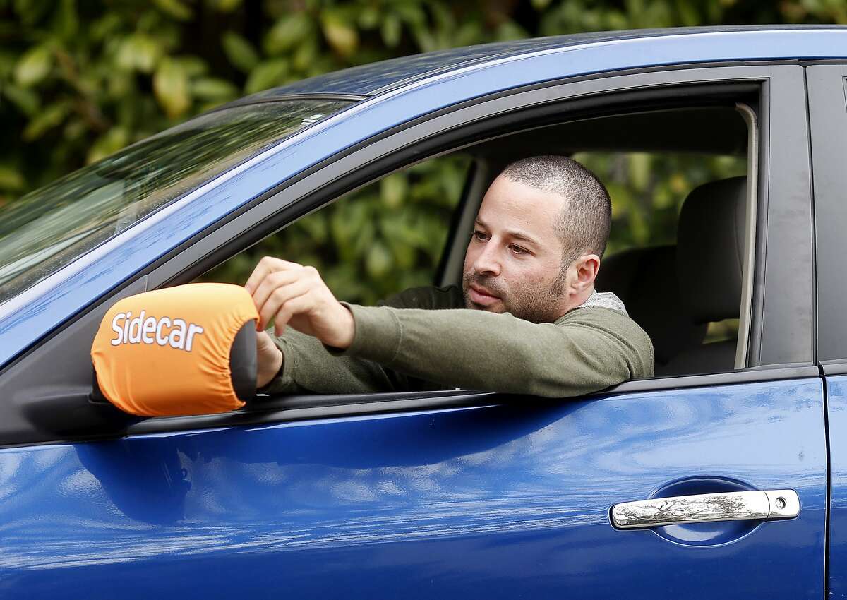 Yonatan Schkolnik adjusts his Sidecar identification bib around his side view mirror Monday November 10, 2014. Yonatan Schkolnik drives paying customers for Sidecar and delivers groceries for Instacart in the Bay Area.